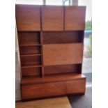 A teak display unit with three cupboard doors over shelving with drop down drinks cabinet over two