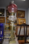 An impressive Victorian oil lamp having cranberry glass shade,clear reservoir and ornate brass