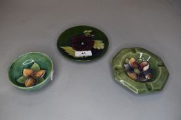 Three vintage pieces of Moorcroft all having green ground included are an ash tray, a pin dish