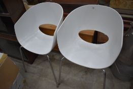 A pair of modernist designer style chairs having chrome legs and white perspex seats