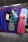 An assortment of colourful ladies dresses, predominantly 1970s, mixed sizes and styles.