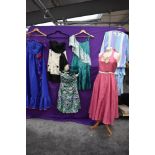 An assortment of colourful ladies dresses, predominantly 1970s, mixed sizes and styles.