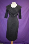 A 1950s black dress having fitted skirt and large portrait collar with bow to front.