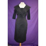 A 1950s black dress having fitted skirt and large portrait collar with bow to front.