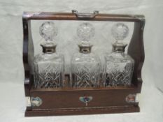 A 20th Century oak tantalus having three cut glass square decanters with silver collars,