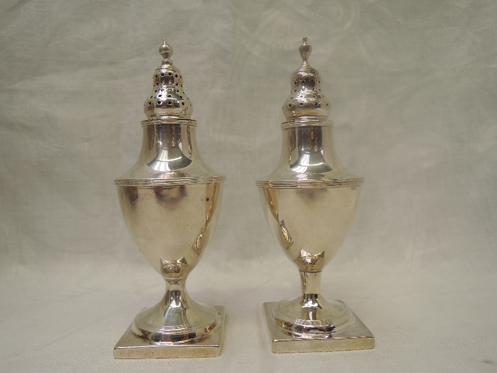 A matched pair of Georgian silver pepper casters of urn form with pierced push on lids and square