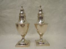A matched pair of Georgian silver pepper casters of urn form with pierced push on lids and square