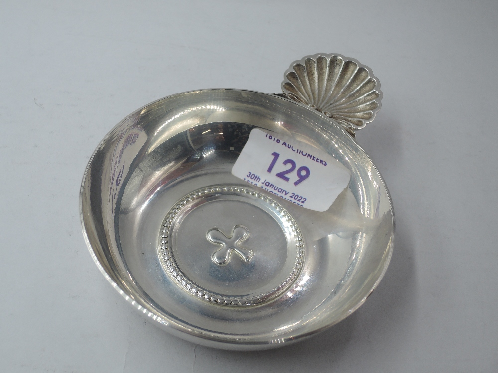 A white metal wine taster of traditional circular form having moulded scallop shell handle, bears