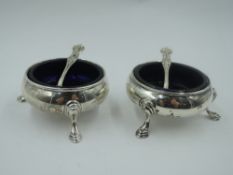 A pair of Victorian silver salts of traditional plain form having trefoil hoof feet and blue glass