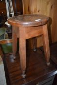 An early 20th century elm stool having circular top on splay legs