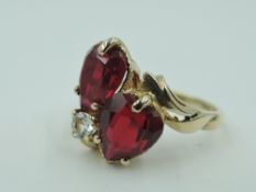 A dress ring having two ruby style teardrop stones in claw set heart mounts with a clear paste stone