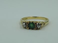 A three stone dress ring having a central emerald flanked by two old cut diamonds in a scrolled