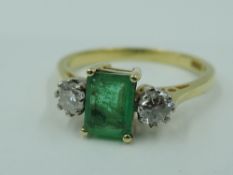 An emerald and diamond dress ring having a central emerald cut emerald flanked by two diamonds in