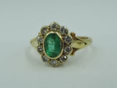 An emerald and diamond oval cluster ring in collared mounts to shaped shoulders on an 18ct gold