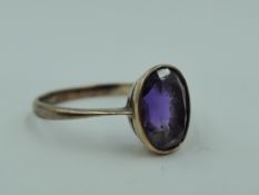 A small oval amethyst dress ring in a collared mount on a rose gold loop, marks worn tests as 9ct