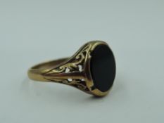 A 9ct gold signet ring having oval black panel in pierced scrolled mount on 9ct gold loop, size