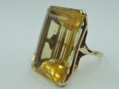 An oversized yellow metal dress ring having a large emerald cut citrine style stone in a claw set