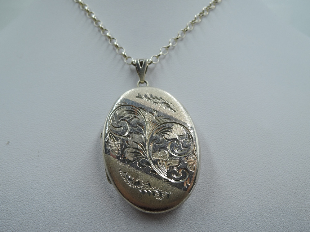 A silver locket of oval form having engraved scroll decoration and silver belcher chain, approx 21.