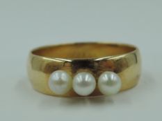 A small converted yellow metal wedding band having three attached seed pearls, hallmarks warn, tests