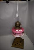 A Victorian oil lamp having pink fade glass well decorated with flowers on cast base