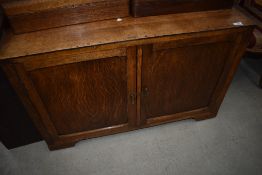 An early 20th Century golden oak low cupboard, having castors