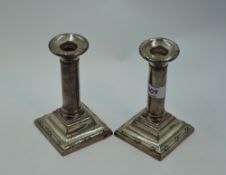 A pair of silver candle sticks of short form having plain columns to weighted square bases with reid