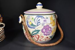 A Poole Pottery hand-decorated biscuit barrel, with finial topped cover and rattan over handle,