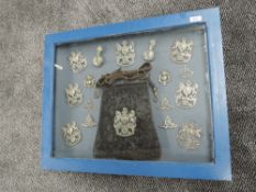 A framed and glazed display case containing Military Helmet & Cap Badges plus a Sabretaches,