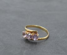 An amethyst trilogy ring having crossover shoulders on a yellow metal band stamped 18K, size R &