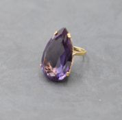 An over sized synthetic Alexandrite pear shaped solitaire ring in a 4 claw set yellow metal basket