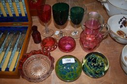 A selection of cranberry glass wares and two Mdina art glass paper weights