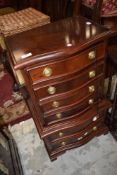 A reproduction hardwood small serpentine chest on chest