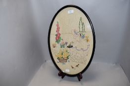 A 1930's embroidered panel, of oval form with crinoline lady within a garden setting, ebonised frame
