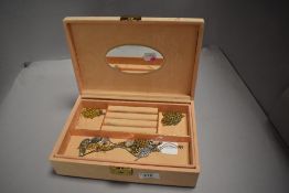 A peach coloured jewellery box containing a selection of costume jewellery chains and necklaces