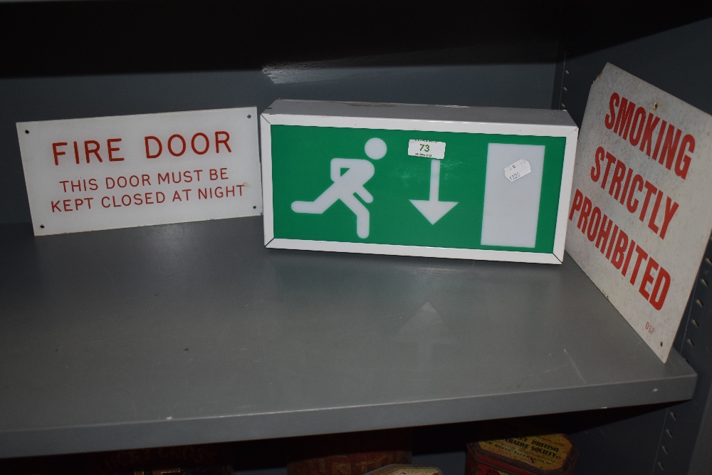 A fire escape light box, no smoking sign and a fire door exit sign.
