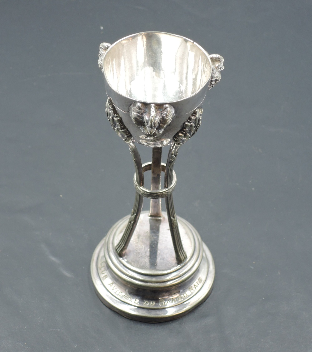 A continental white metal trophy, of half-egg form with cockerel mask ornaments, supported by