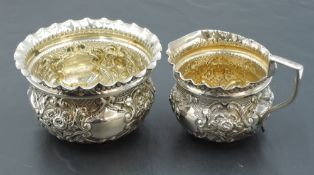 A late Victorian cased silver sugar and cream, embossed with foliate decoration and black