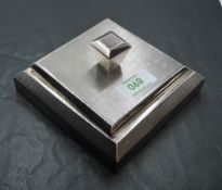 An Art Deco silver table powder box of square form having engine turned decoration, bakelite base