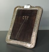 A silver rectangular photograph frame having arched top and hammered finish with wooden easel stand,