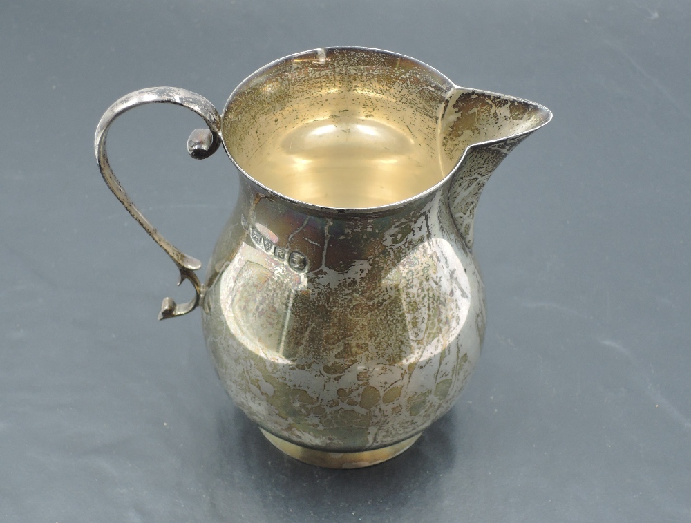 A silver cream jug of plain baluster form having loop handle and pedestal foot, Chester 1935, S