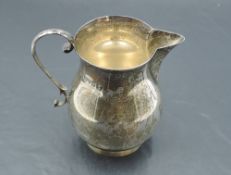 A silver cream jug of plain baluster form having loop handle and pedestal foot, Chester 1935, S