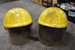 Two modern fireman helmets with fold down visors both having seen action