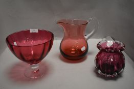 A selection of cranberry glass wares including footed comport and water jug