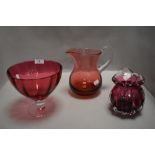A selection of cranberry glass wares including footed comport and water jug