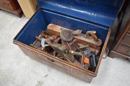 A vintage tin trunk with wood grain decoration containing a selection of hand tools including