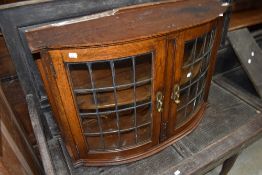 An Arts and Crafts period bow fronted oak wall cabinet, the shaped doors each with multiple convex