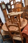 A rustic pine circular dining table and set of six ladderback chairs having rush seats
