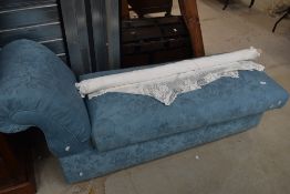 A modern chaise long upholstered in a blue fabric with fold out seat for storage