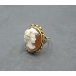 A conch shell cameo ring depicting a bacchanalian maiden in profile in a collared mount on a