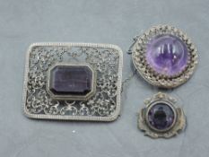 A white metal and amethyst brooch, with central emerald-cut amethyst within a pierced C-scroll